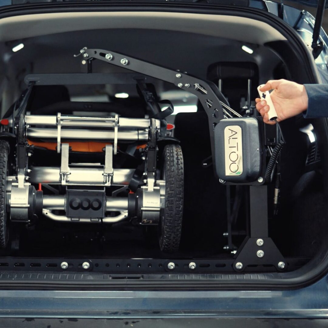 Utilisateur commandant la grue Altoo avec la manette filaire — SmartChair Travel Max chargé dans le coffre d'un SUV bleu — Acekare