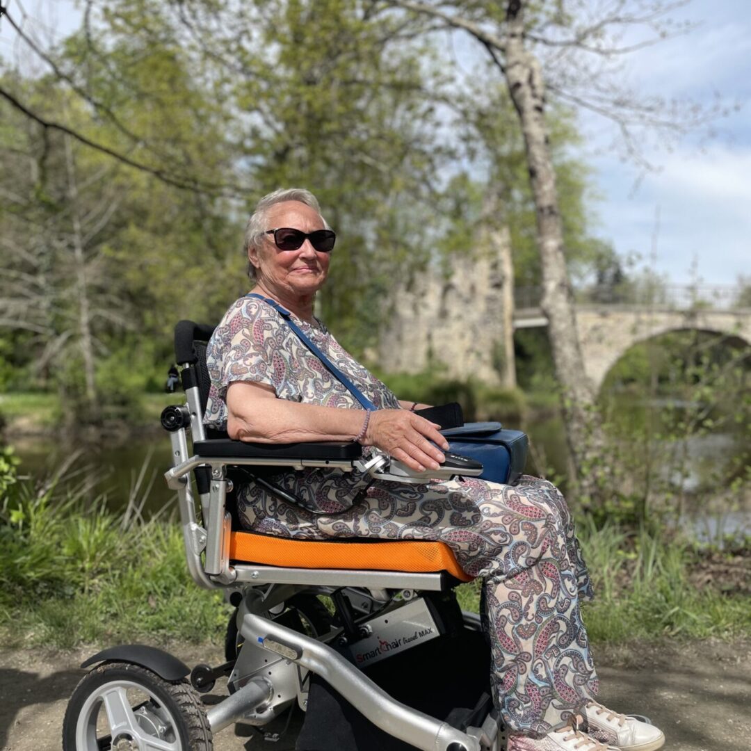 Yvette utilisant le SmartChair Travel Max - fauteuil roulant électrique pliable offrant autonomie et confort. Parfait pour retrouver une mobilité optimale.